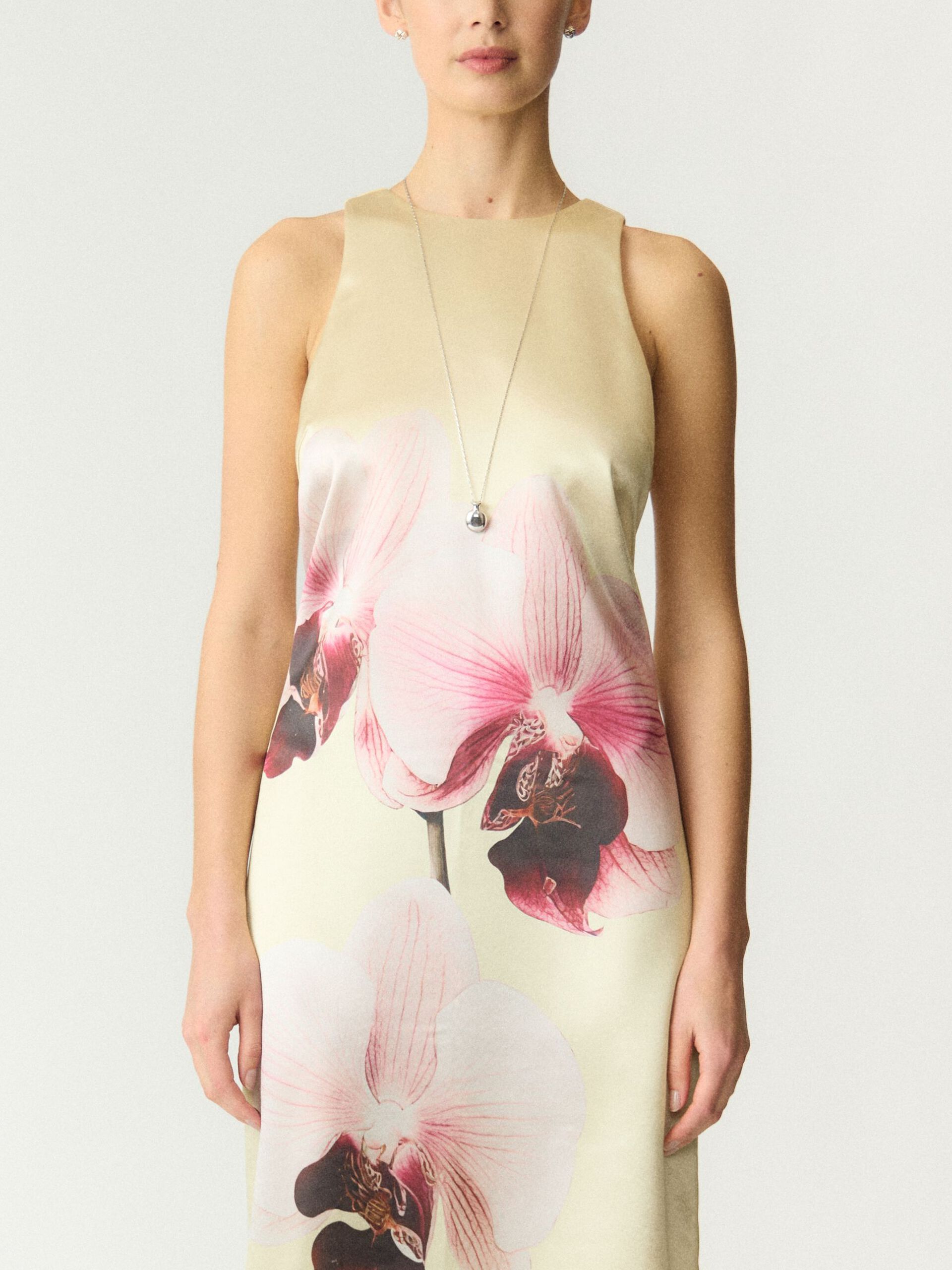 Woman wearing a sleeveless dress with floral design on a plain background