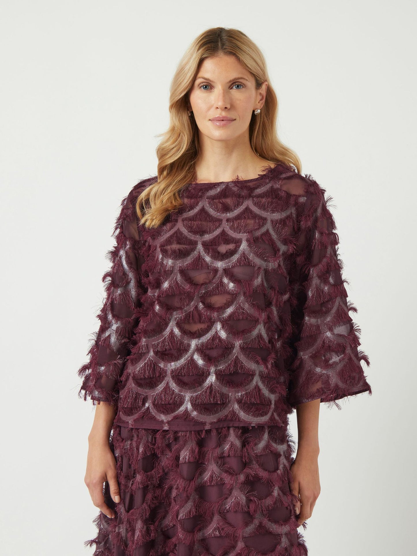 Woman wearing a burgundy lace top and skirt with a white background