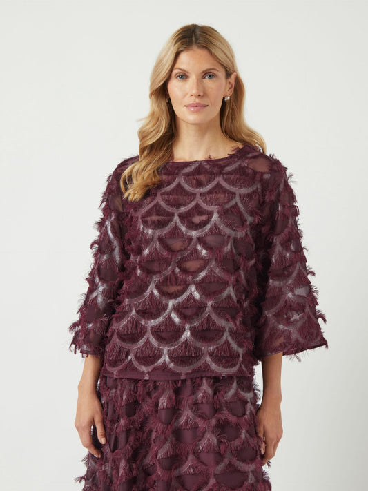 Woman wearing a burgundy lace top and skirt with a white background
