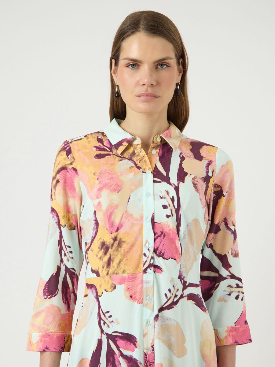 Woman wearing a colorful floral patterned shirt against a white background