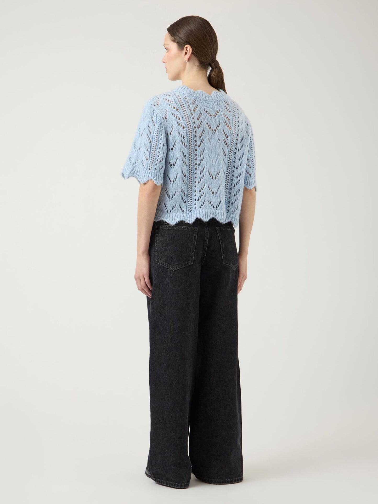 Woman wearing a light blue knitted top and dark jeans on a white background