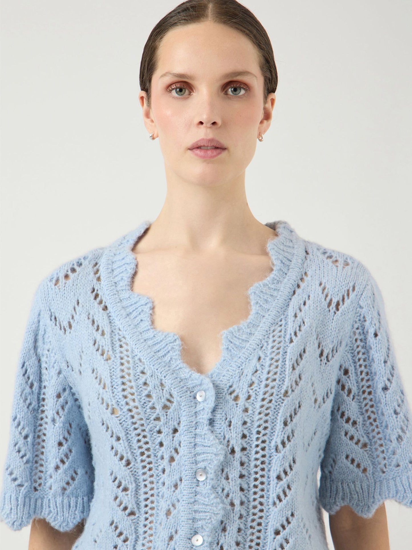 Woman wearing a light blue knitted cardigan against a plain background