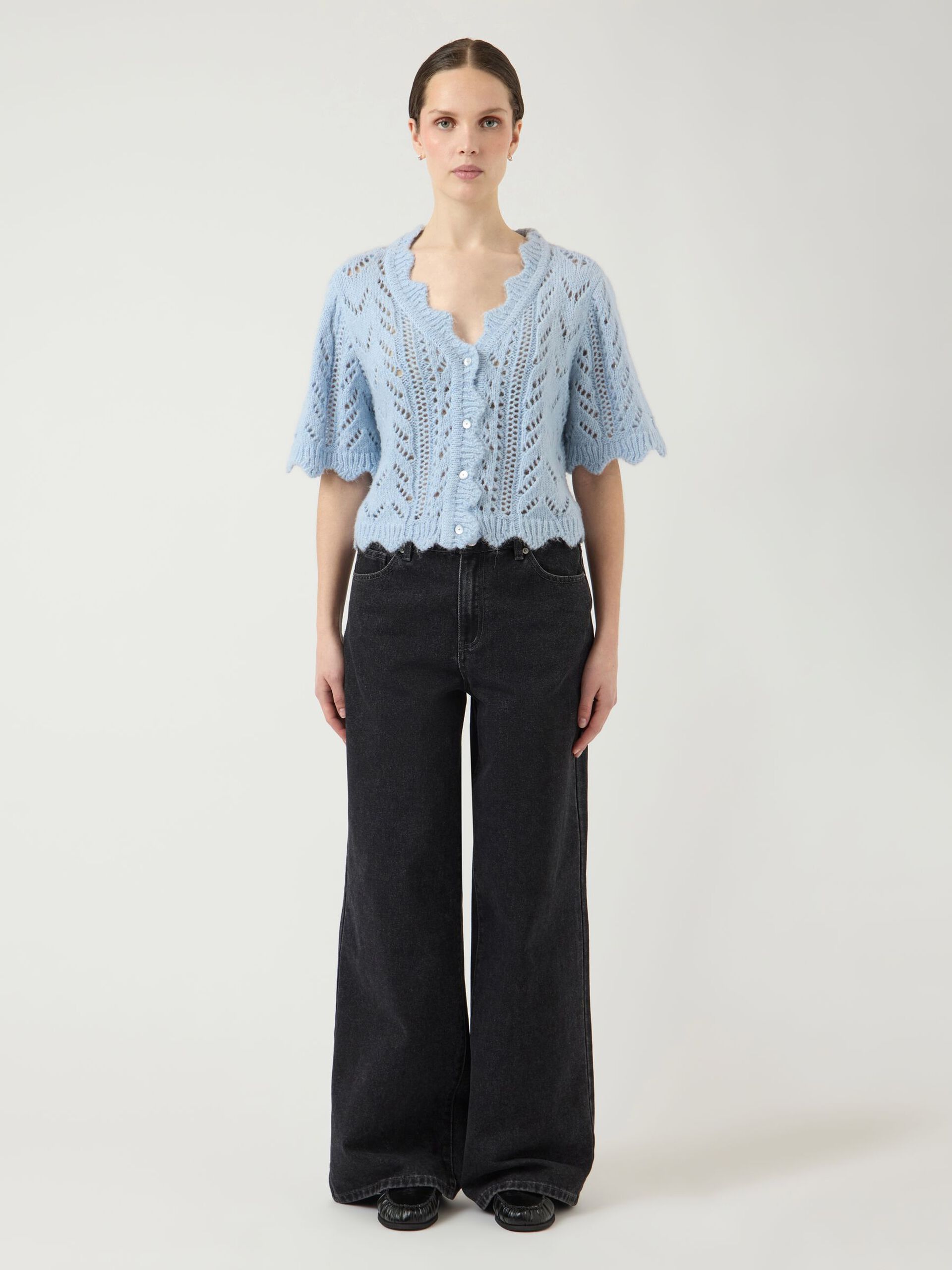 Woman wearing a light blue knitted top and black pants on a white background