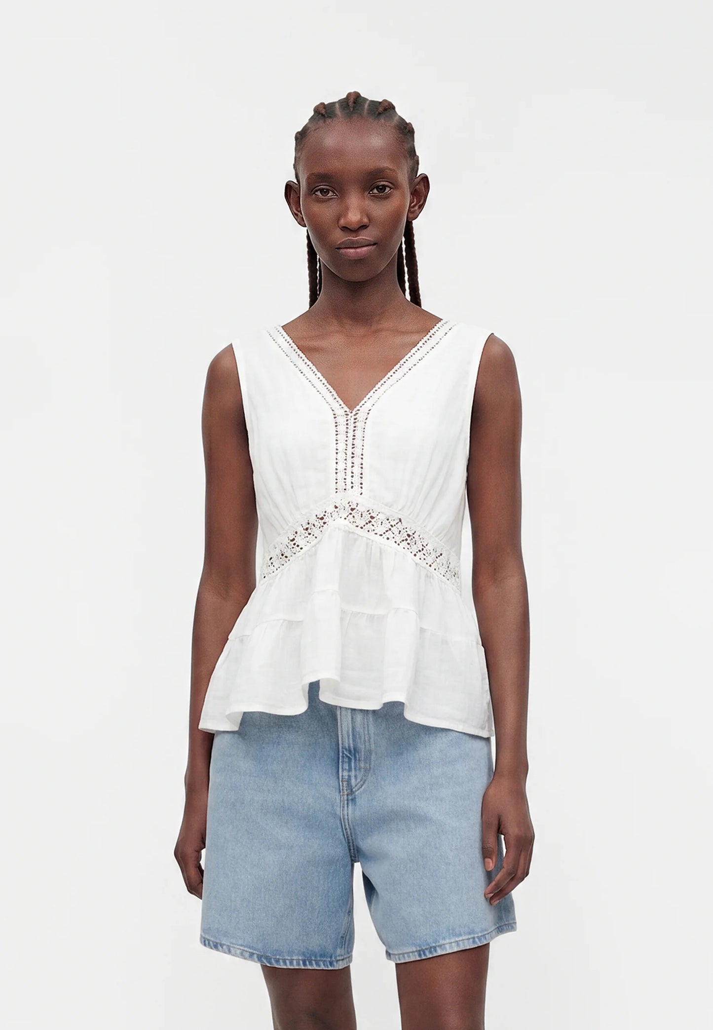 Woman wearing a white sleeveless top with lace details and light blue denim shorts on a white background