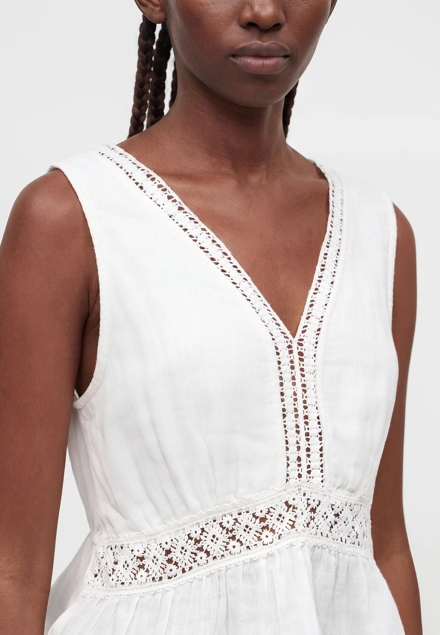White sleeveless dress with lace details worn by a model on a white background