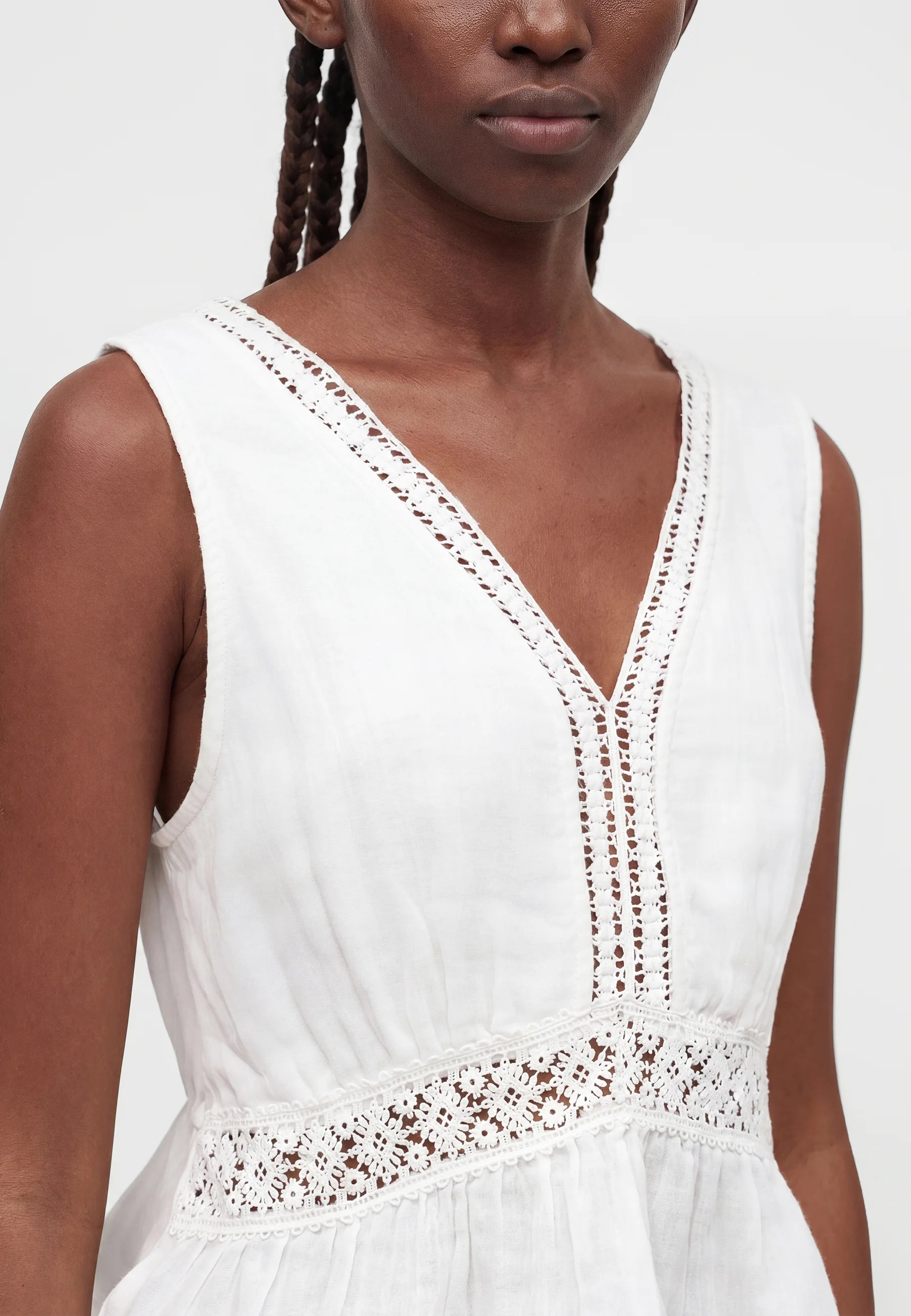 White sleeveless dress with lace details worn by a model on a white background