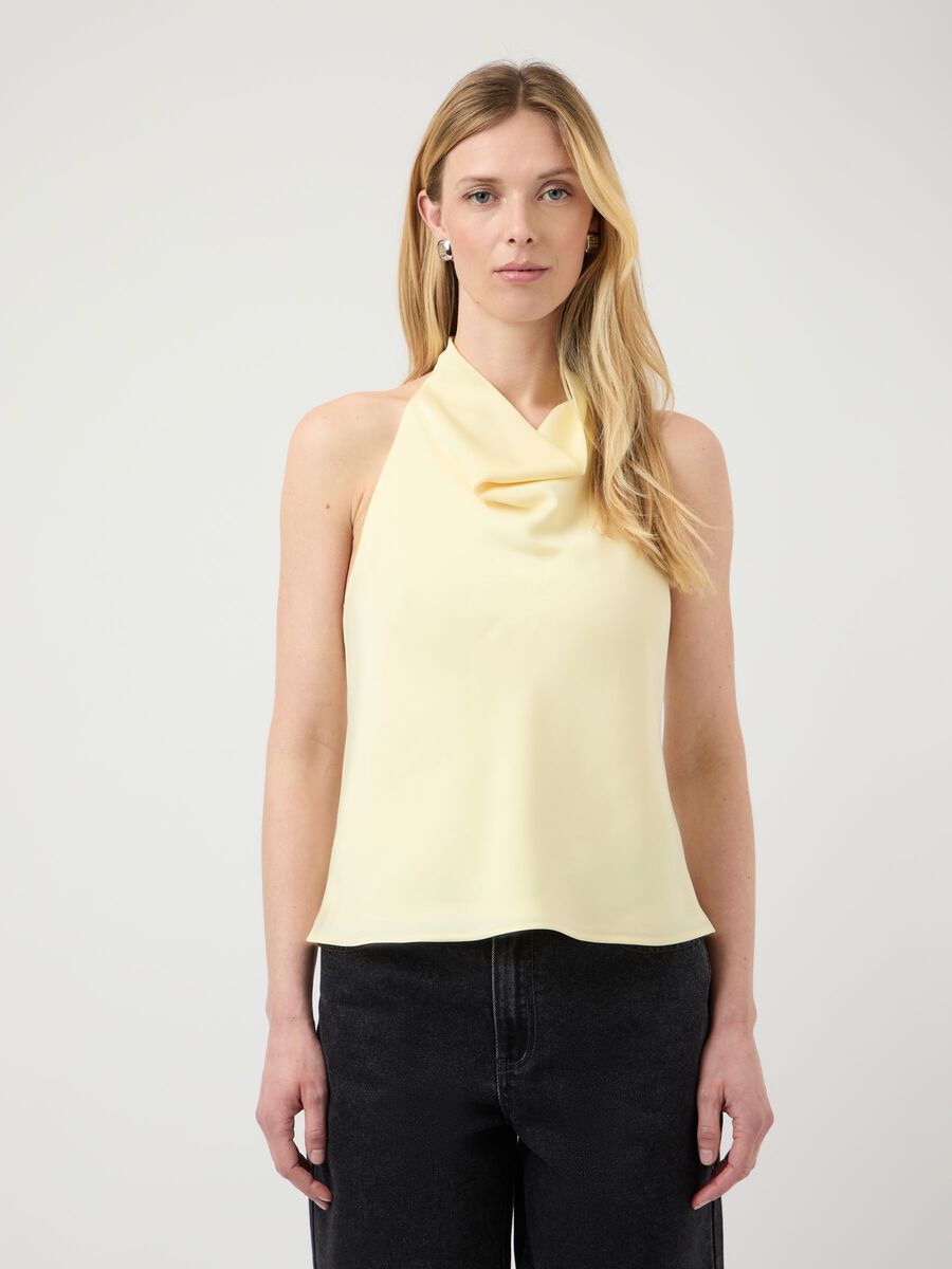 Woman wearing a light yellow sleeveless top with a plain background