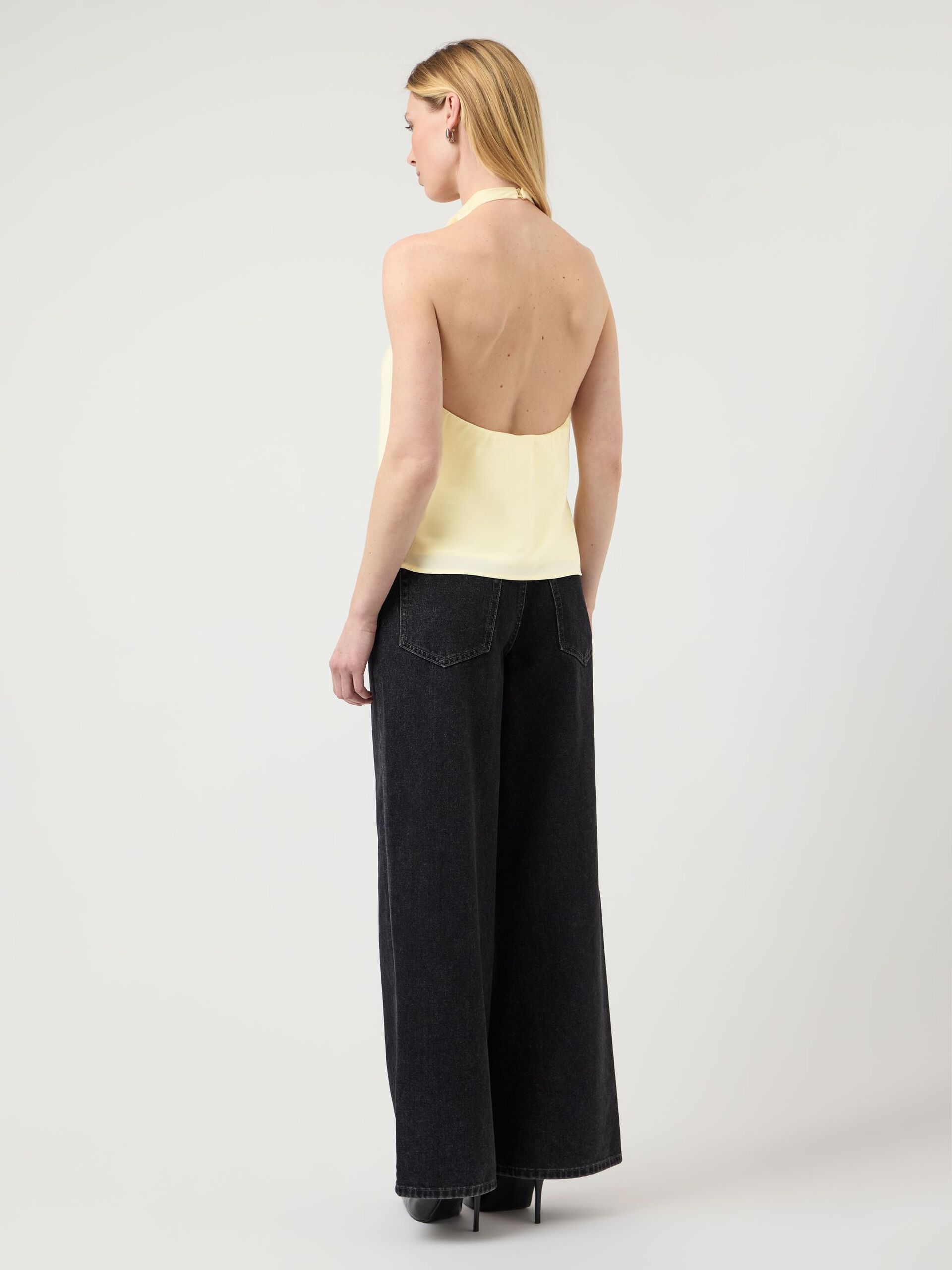 Woman wearing a yellow top and black wide-leg pants on a white background
