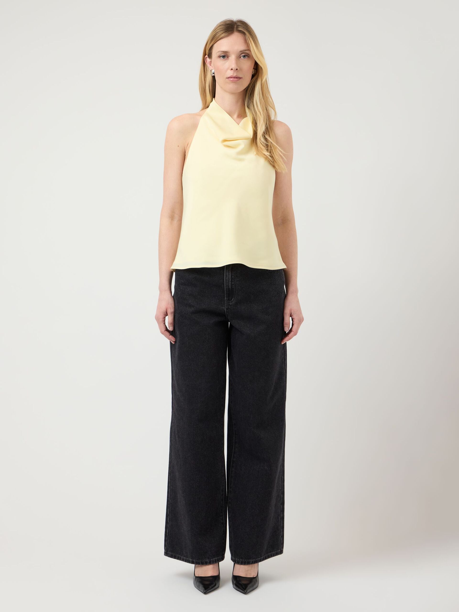 Woman wearing a yellow top and black jeans on a white background