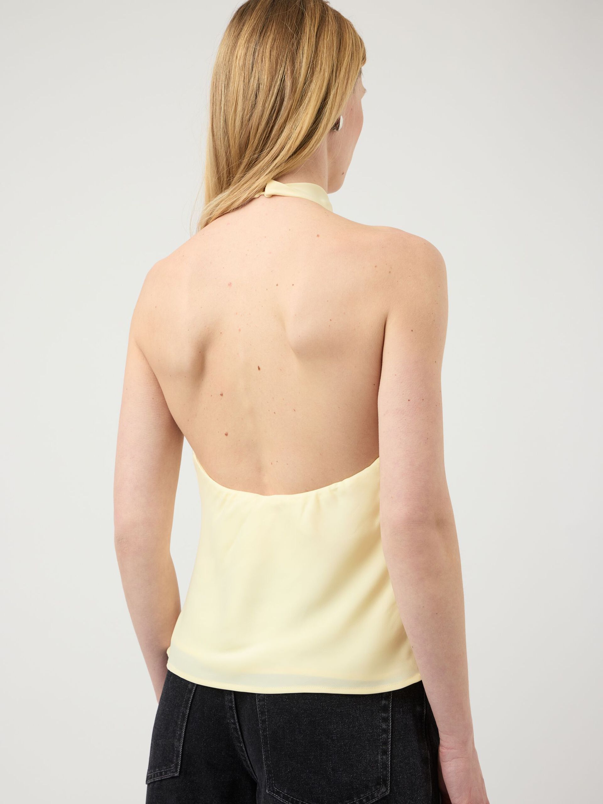 Woman wearing a light yellow halter top against a plain background