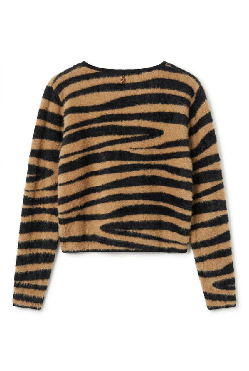 A fuzzy knit sweater with a bold black and tan zebra stripe pattern, hanging on a wooden hanger on a dark display table inside a clothing store.