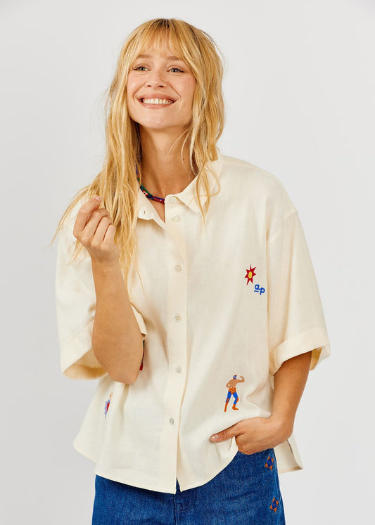 Woman wearing a cream-colored shirt with embroidered designs on a plain background