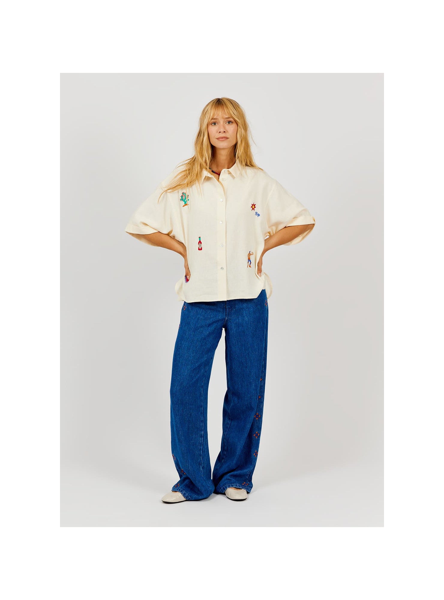 Person wearing a cream-colored shirt with colorful designs and blue jeans on a white background