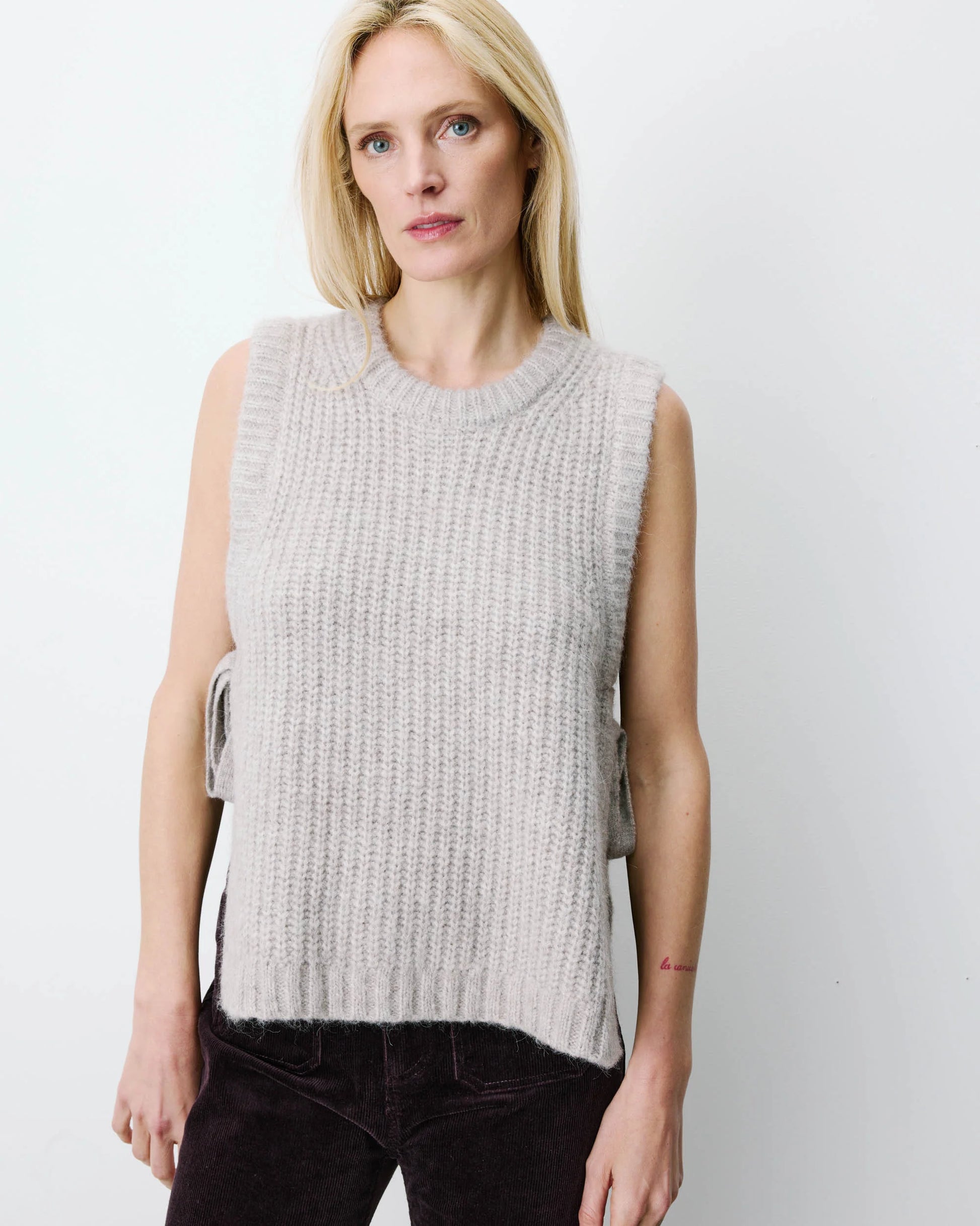 Woman wearing a light gray knitted vest against a white background