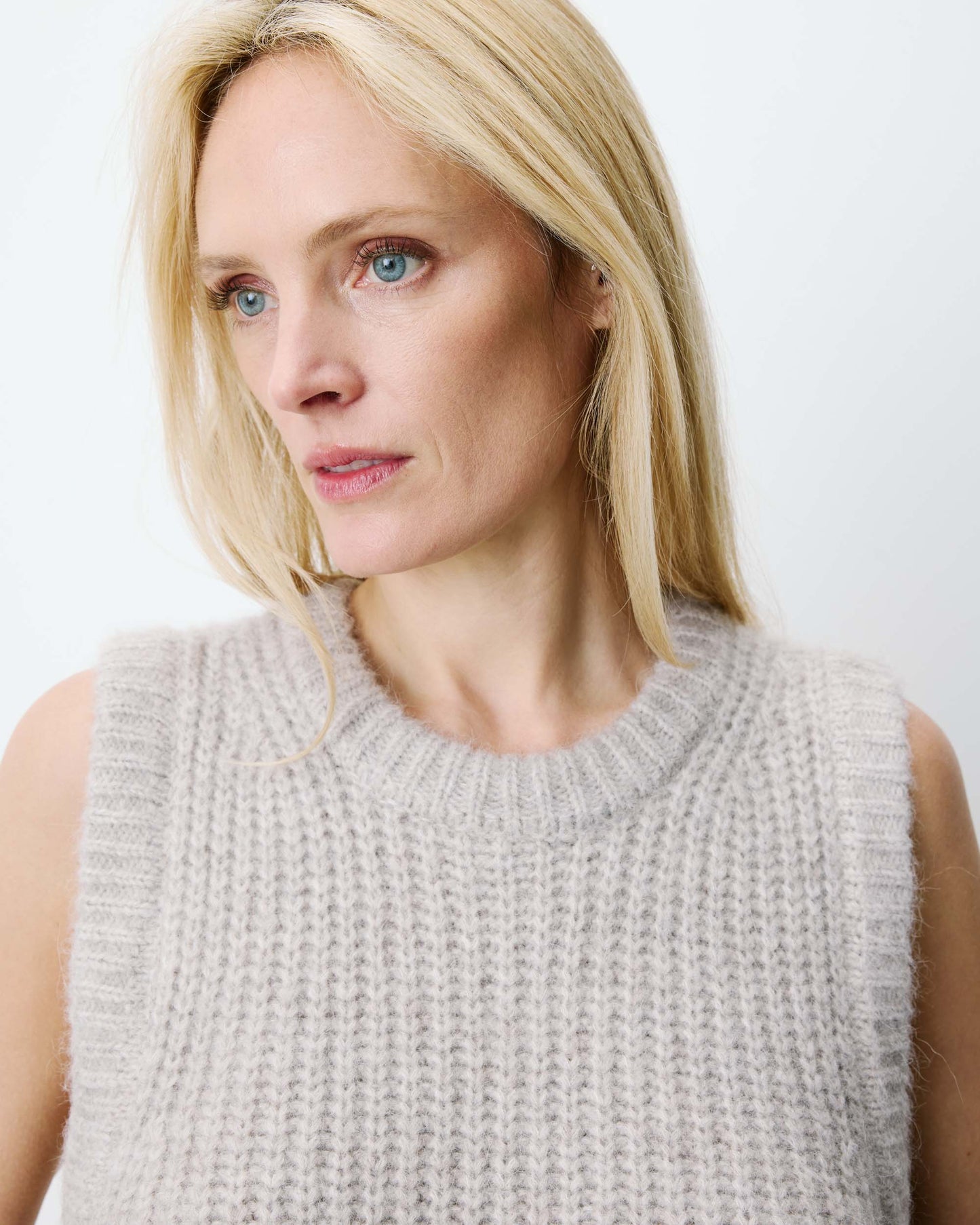 Woman wearing a light gray sleeveless knitted top against a white background