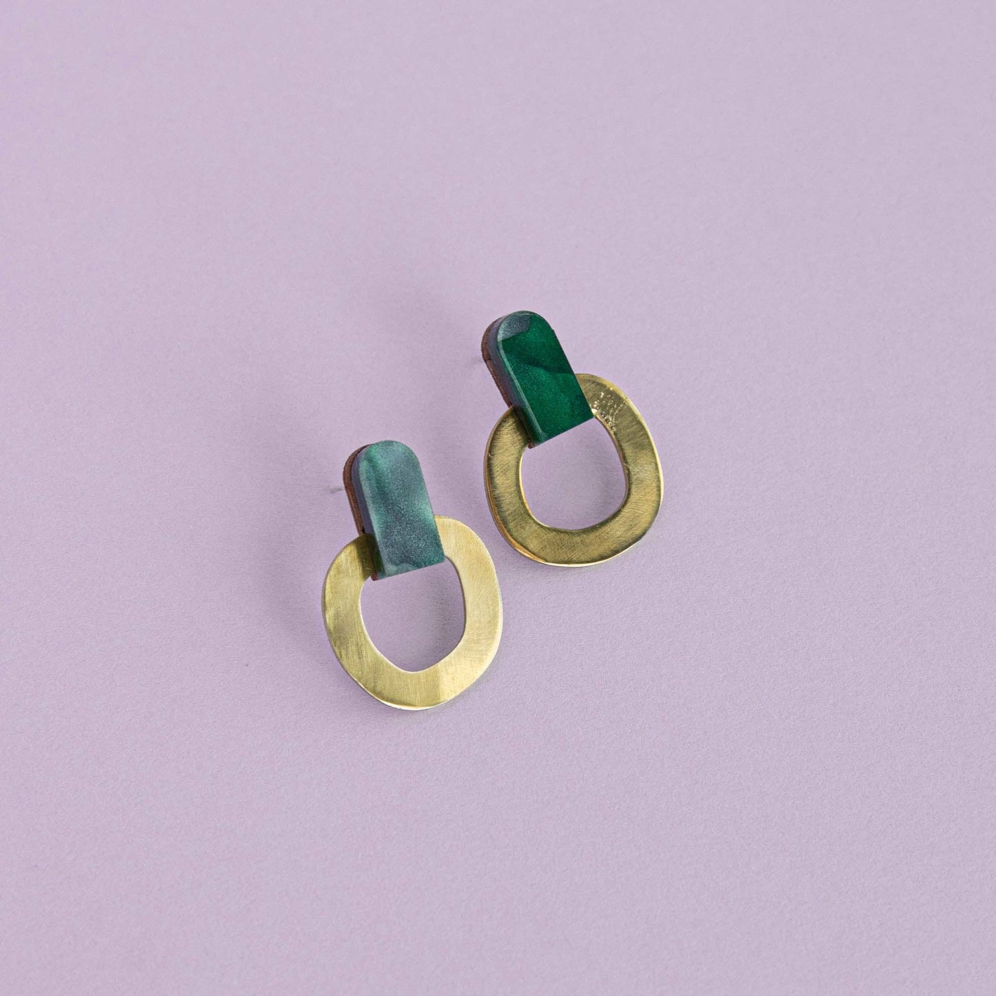 Pair of earrings with green and gold circular designs on a light purple background