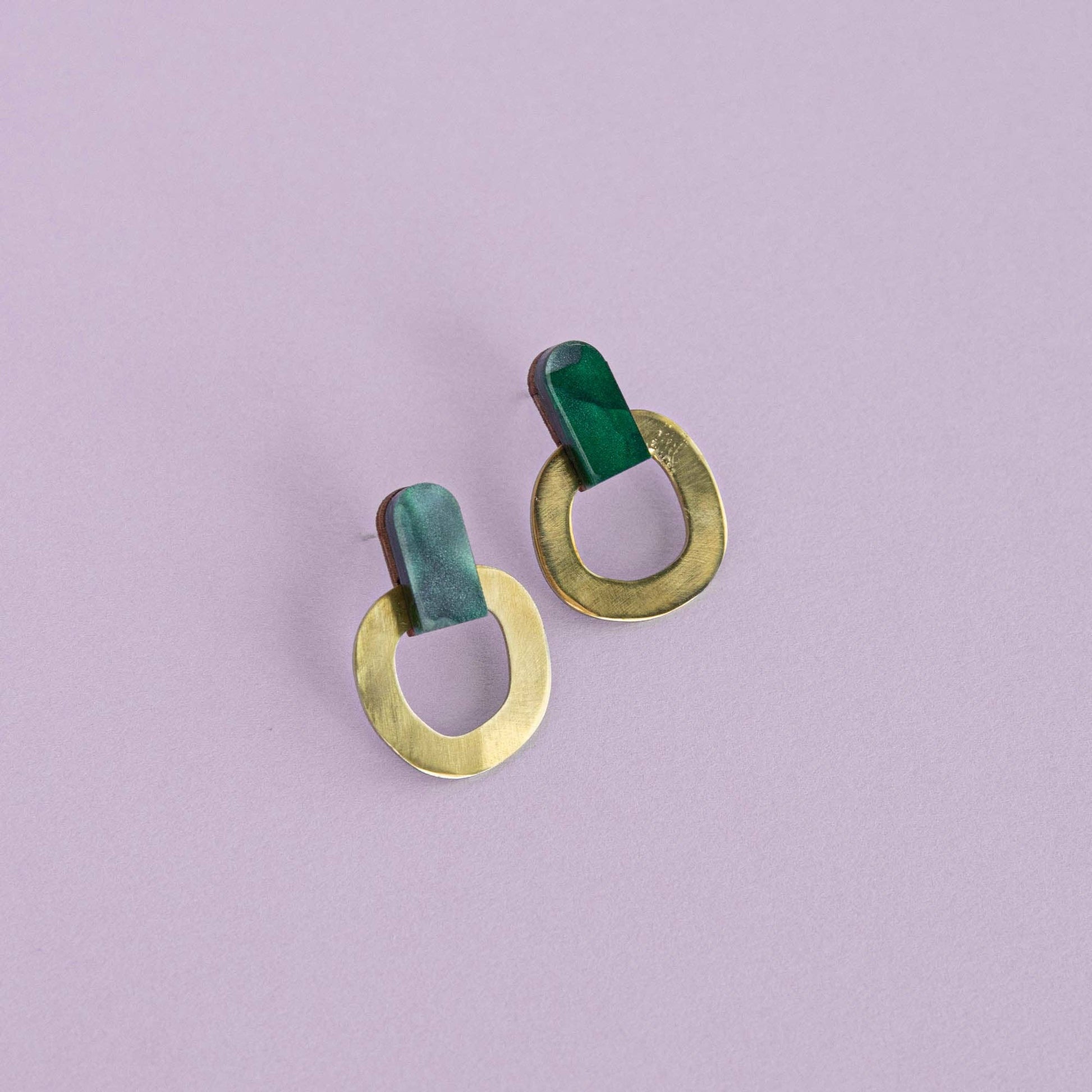 Pair of earrings with green and gold circular designs on a light purple background