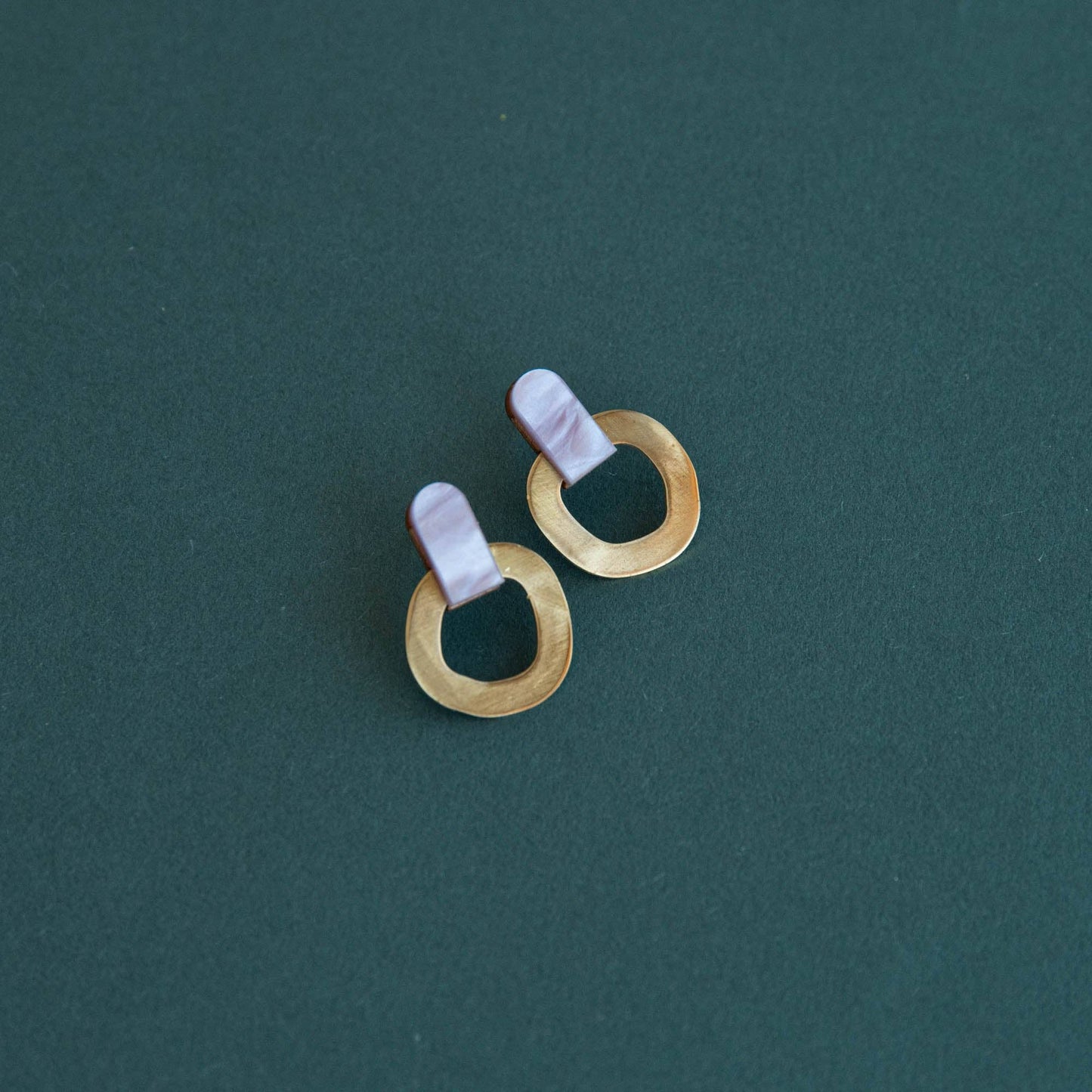 Pair of gold hoop earrings with pink accents on a teal background