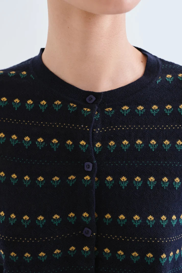 Close-up of a person wearing a dark navy knit cardigan with a repeating small yellow and green floral pattern and a button front.