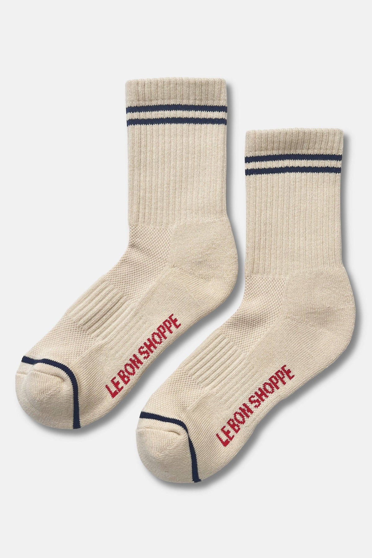 A pair of cream-colored crew socks with navy blue stripes near the cuff and red 'LEBON SHOPPE' branding printed on the sole, displayed against a light gray background.