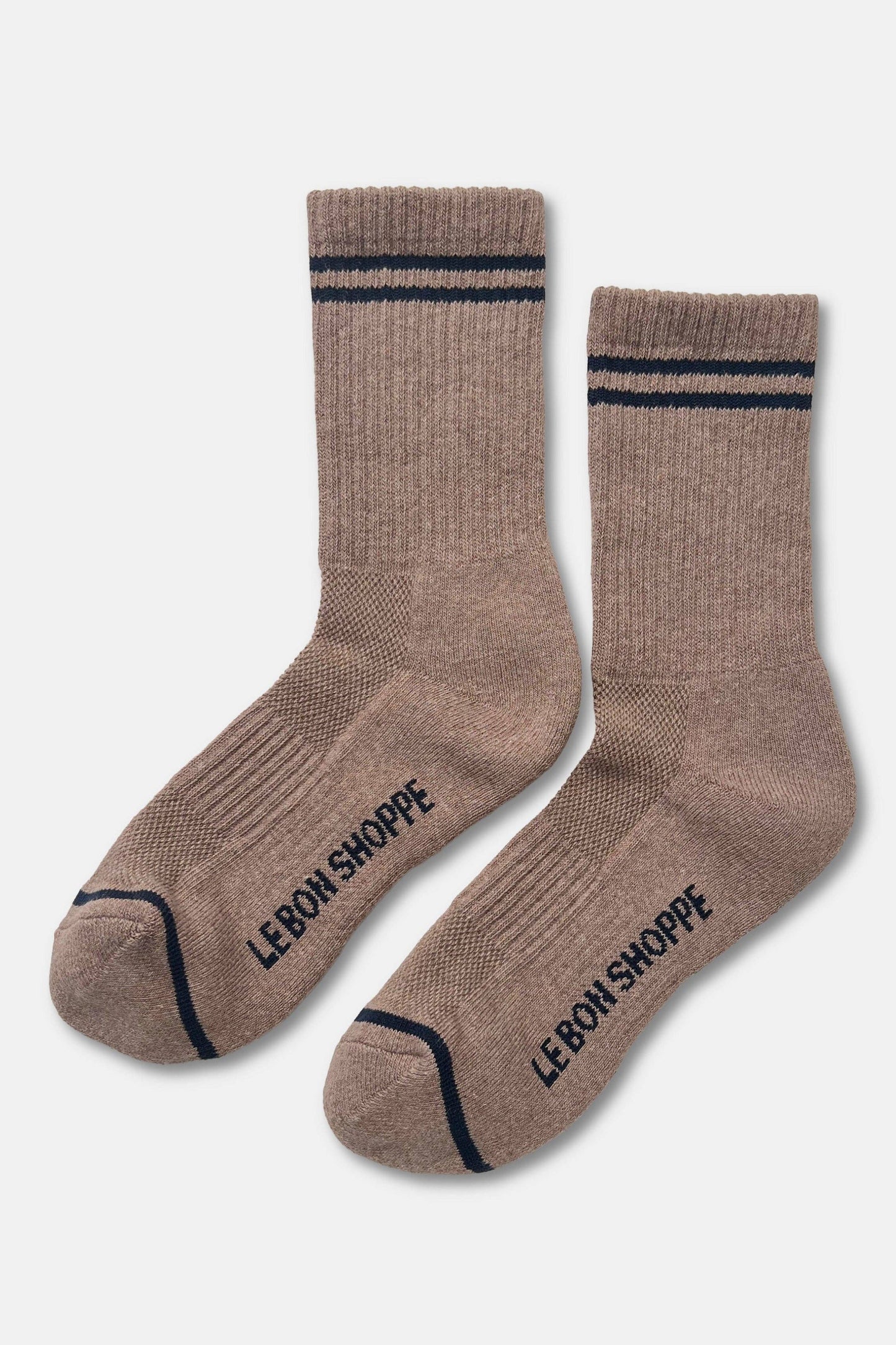 A pair of ribbed crew socks in a warm taupe-brown color, featuring navy blue stripes near the cuffs and the brand name 'LE BON SHOPPE' printed in navy on the sole of each sock, set against a light gray background.