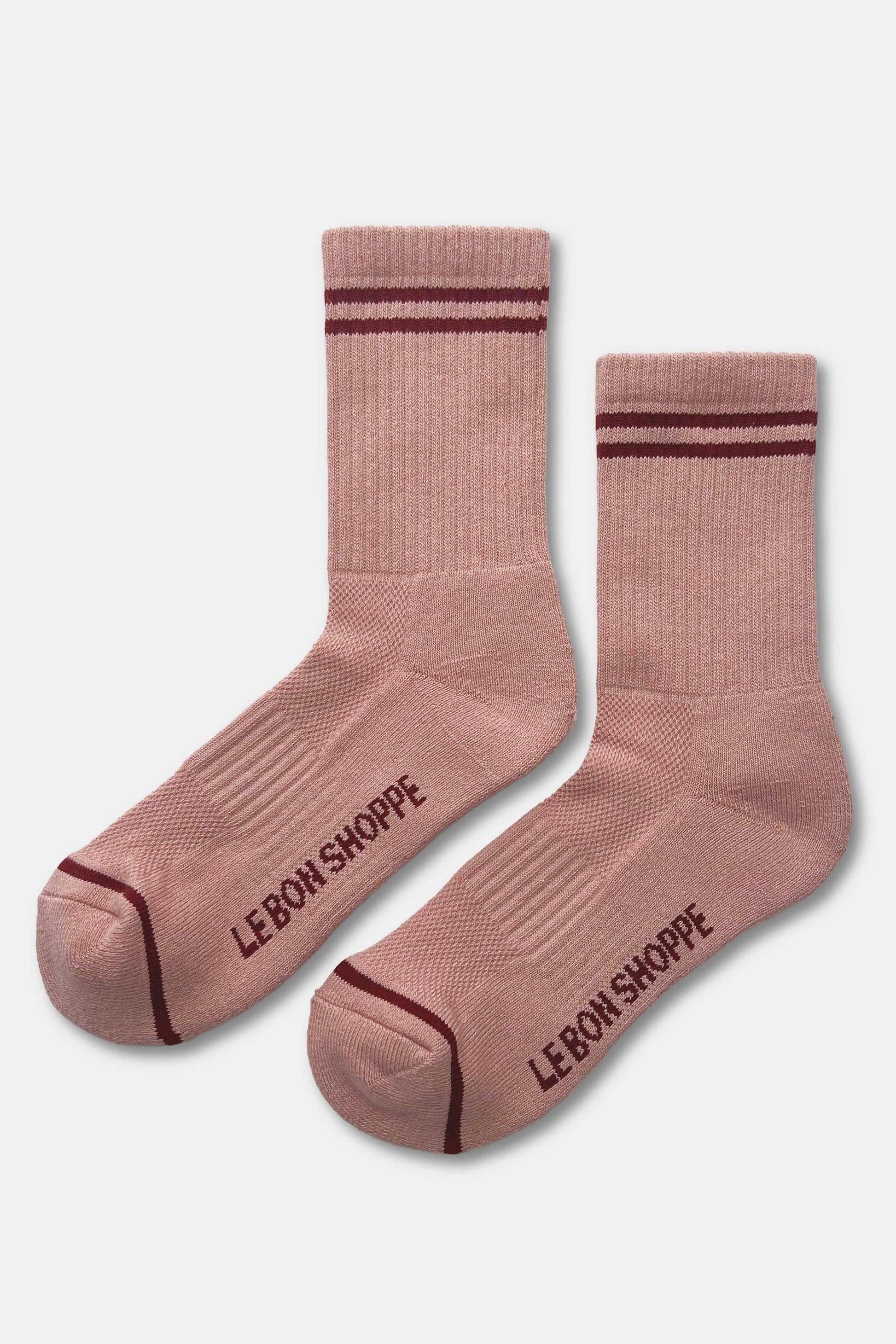 A pair of dusty pink crew socks with dark burgundy stripes near the cuffs and toes, featuring the text 'LE BON SHOPPE' printed on the soles, shown against a light gray background.