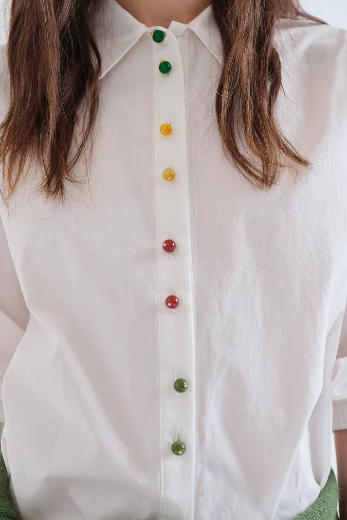 A close-up of a white button-down shirt worn by a person, featuring colorful translucent buttons in green, yellow, and red along the front placket.