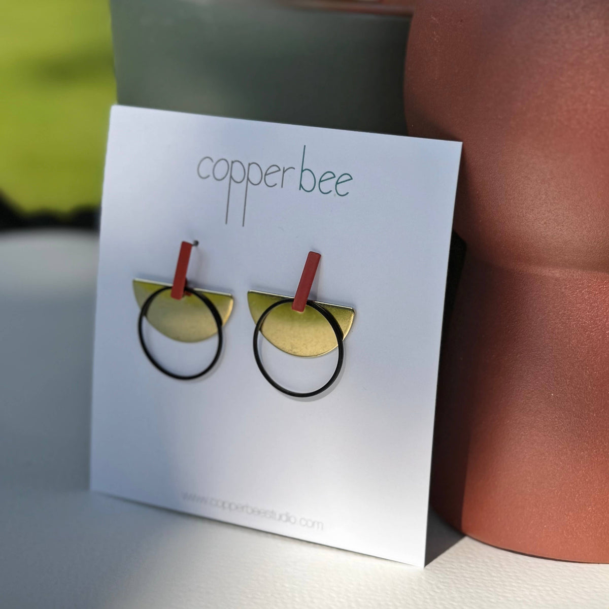Copperbee earrings on a display card with a blurred background