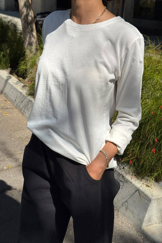 Person wearing a white sweatshirt and dark pants on a sidewalk.