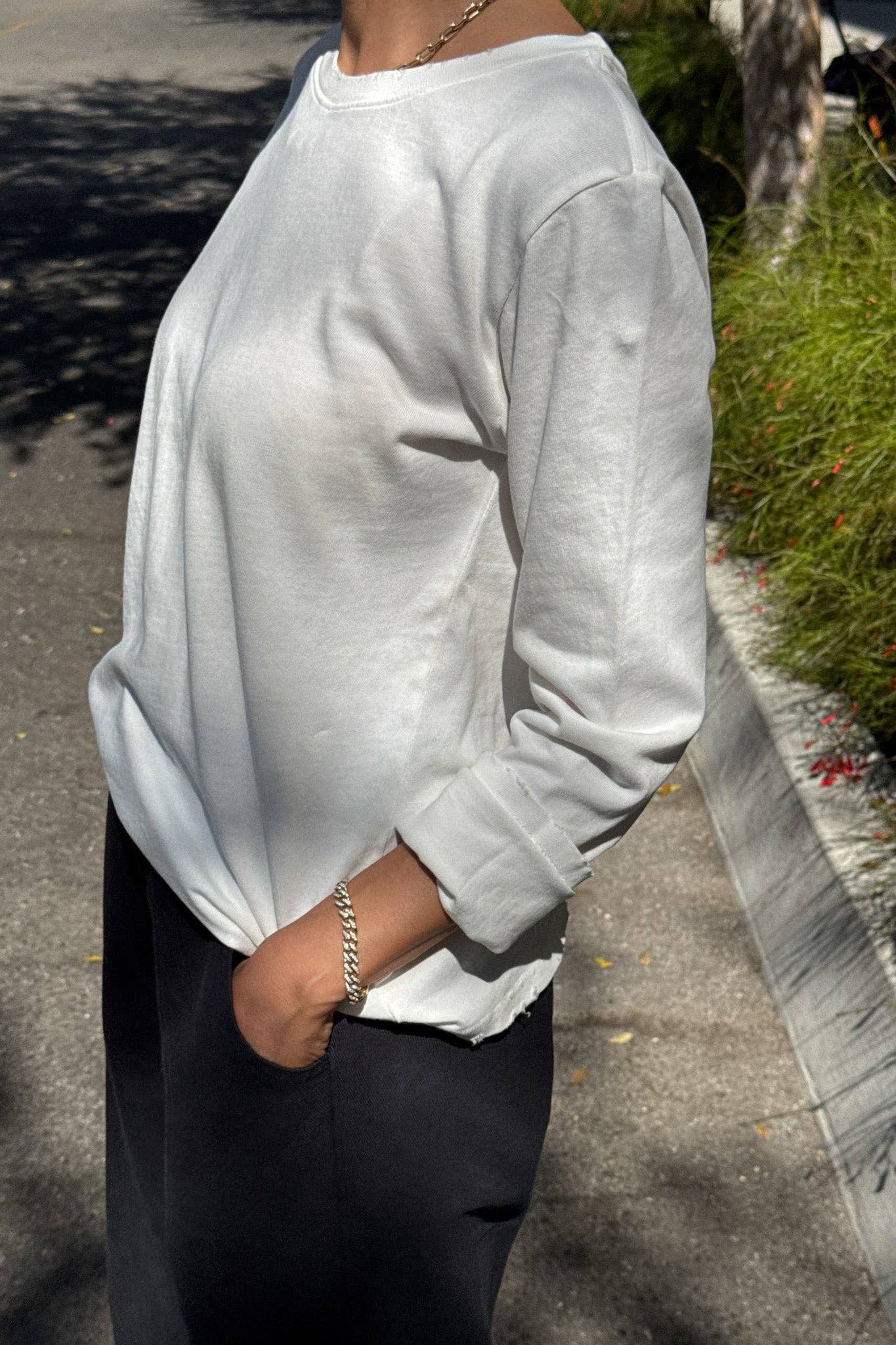 Person wearing a light gray sweatshirt and dark pants on a sidewalk.
