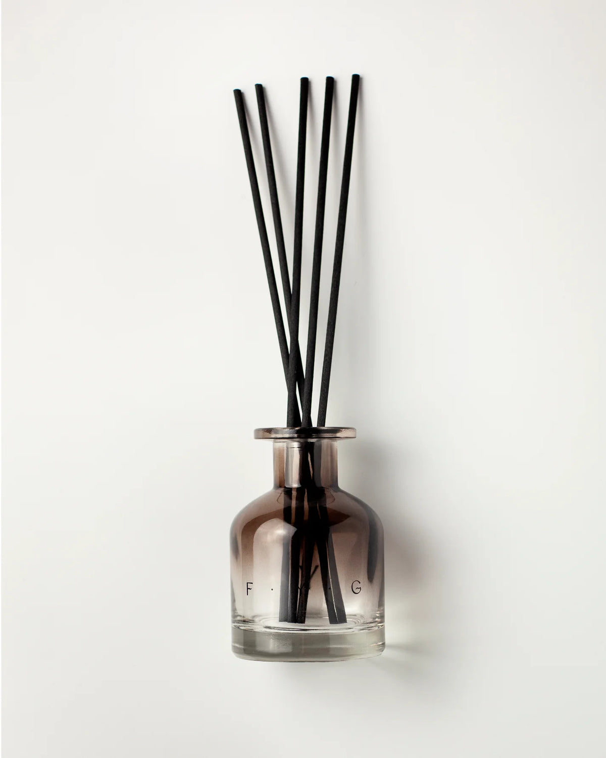 A reed diffuser with a smoky amber glass bottle and six black reeds, set against a plain white background.