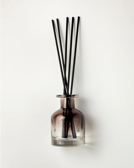 A reed diffuser with a smoky amber glass bottle and six black reeds, set against a plain white background.