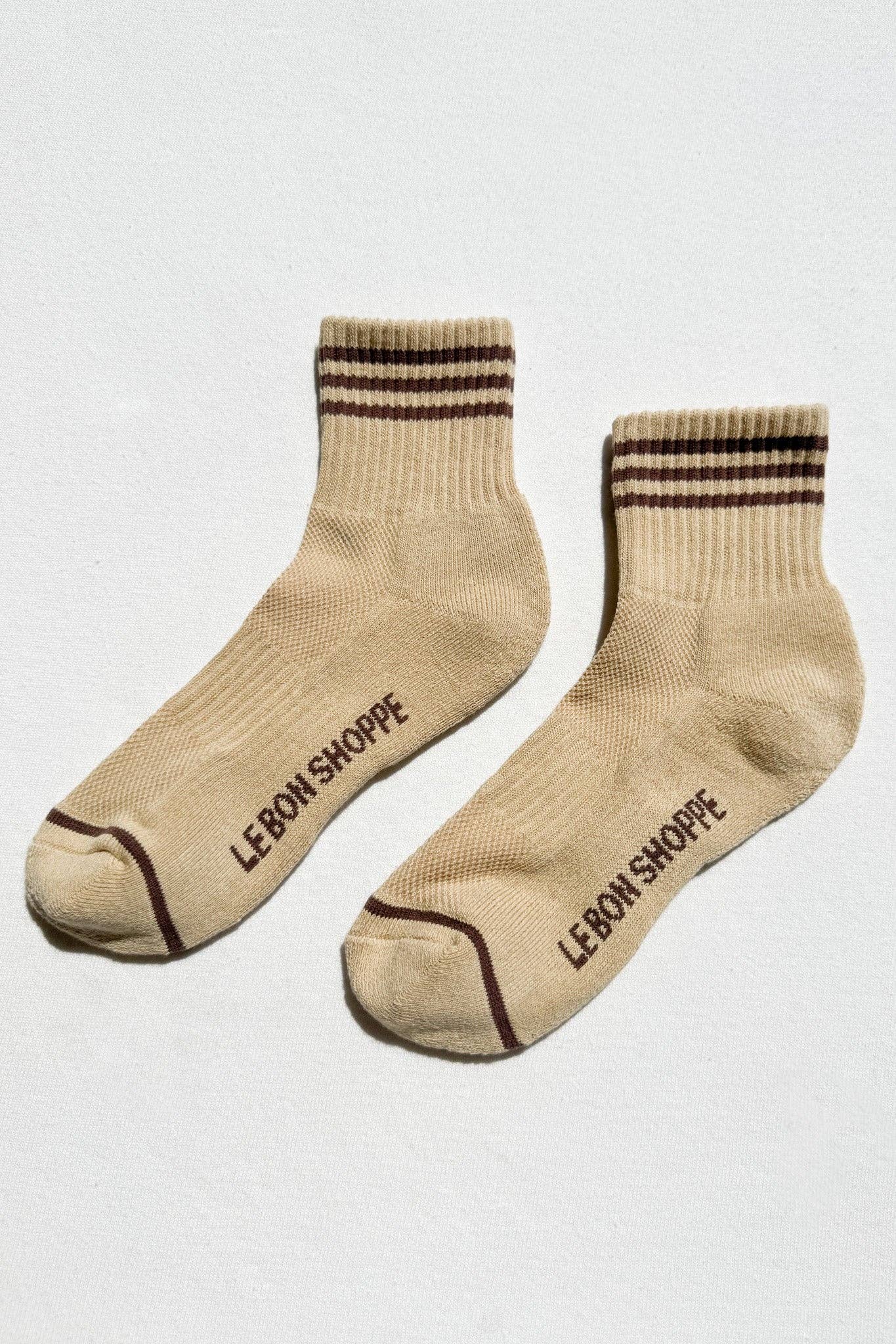 Pair of beige socks with brown stripes and 'Le Bon Shoppe' branding on a light gray background
