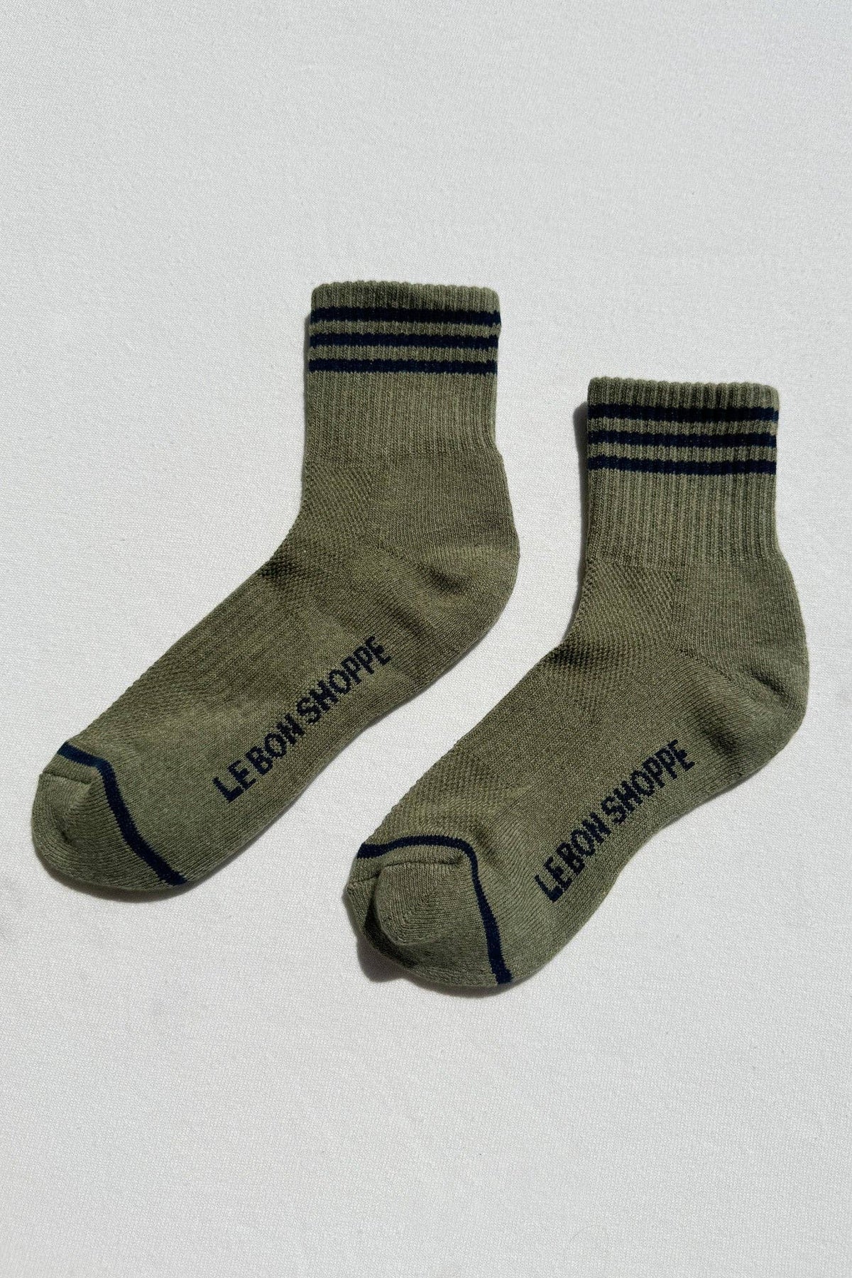 Pair of green socks with black stripes and 'LE-BON SHOPPE' branding on a light gray background