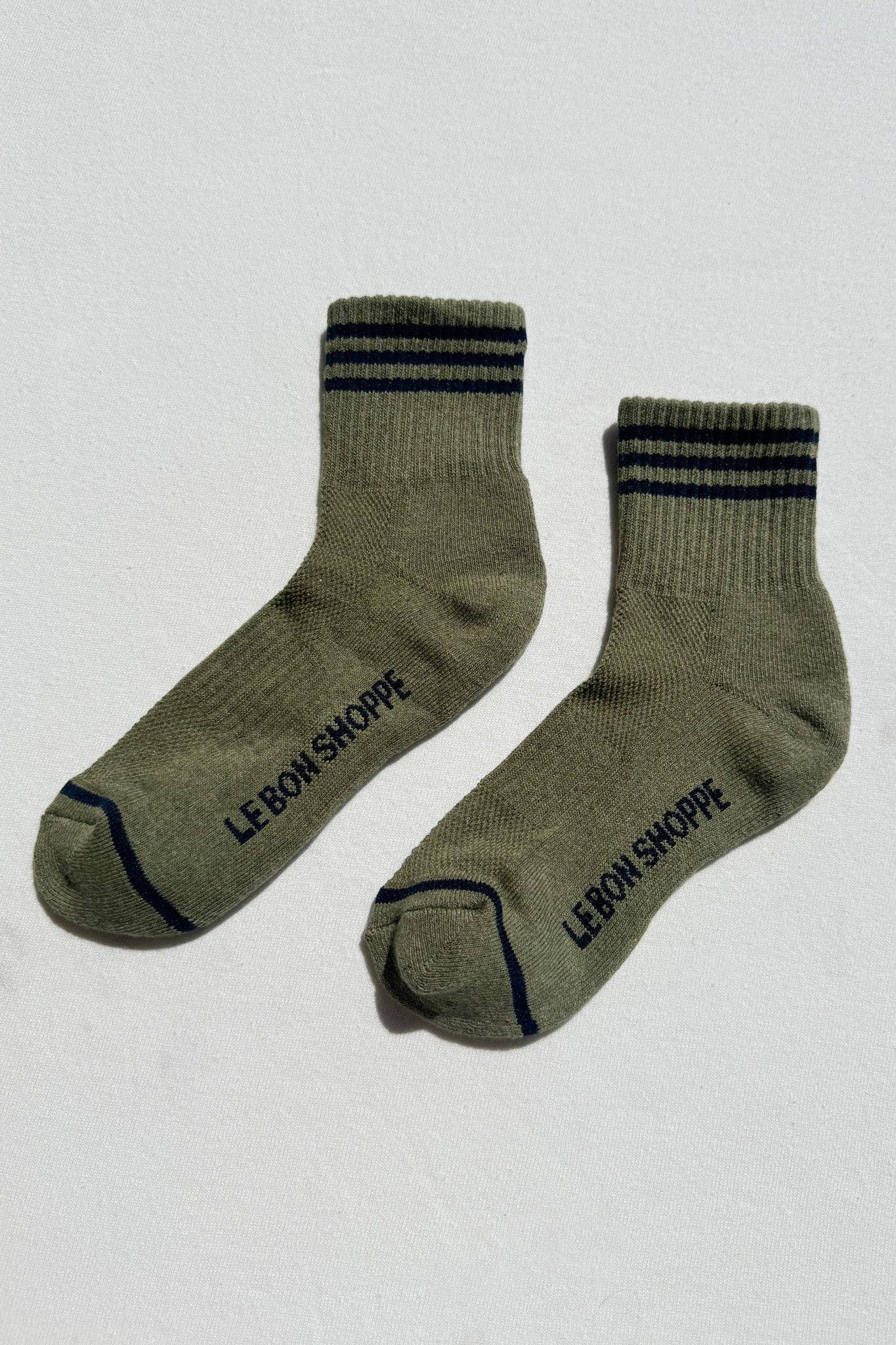 Pair of green socks with black stripes and 'LE-BON SHOPPE' branding on a light gray background
