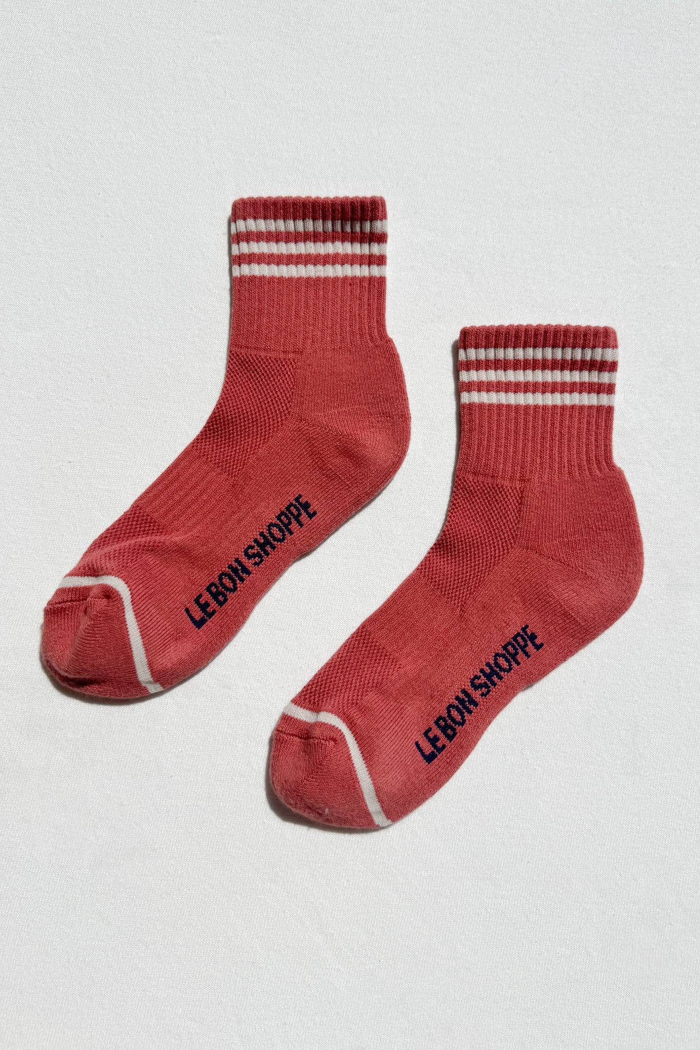 Red socks with white stripes and 'Le Bon Shoppe' branding on a light gray background
