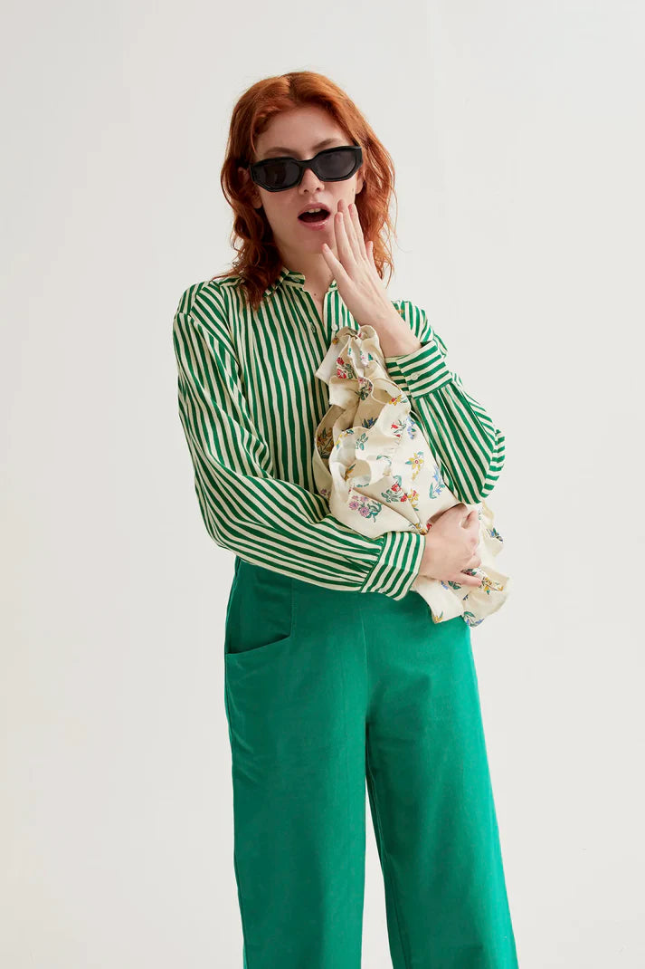 Person wearing a green and white striped shirt with floral pants on a plain background