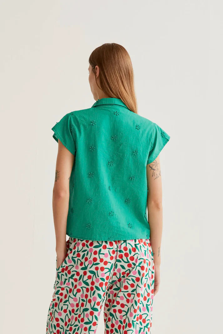 Person wearing a green patterned shirt and colorful pants on a plain background