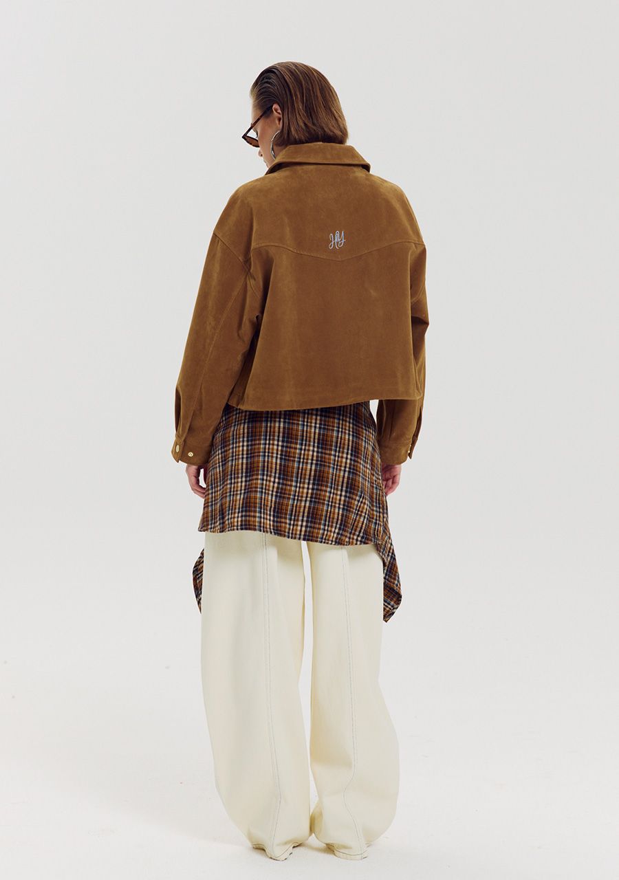 A model is shown from the back wearing a brown cropped suede jacket, a brown and red plaid shirt, and cream wide-leg trousers, against a plain light gray studio background.