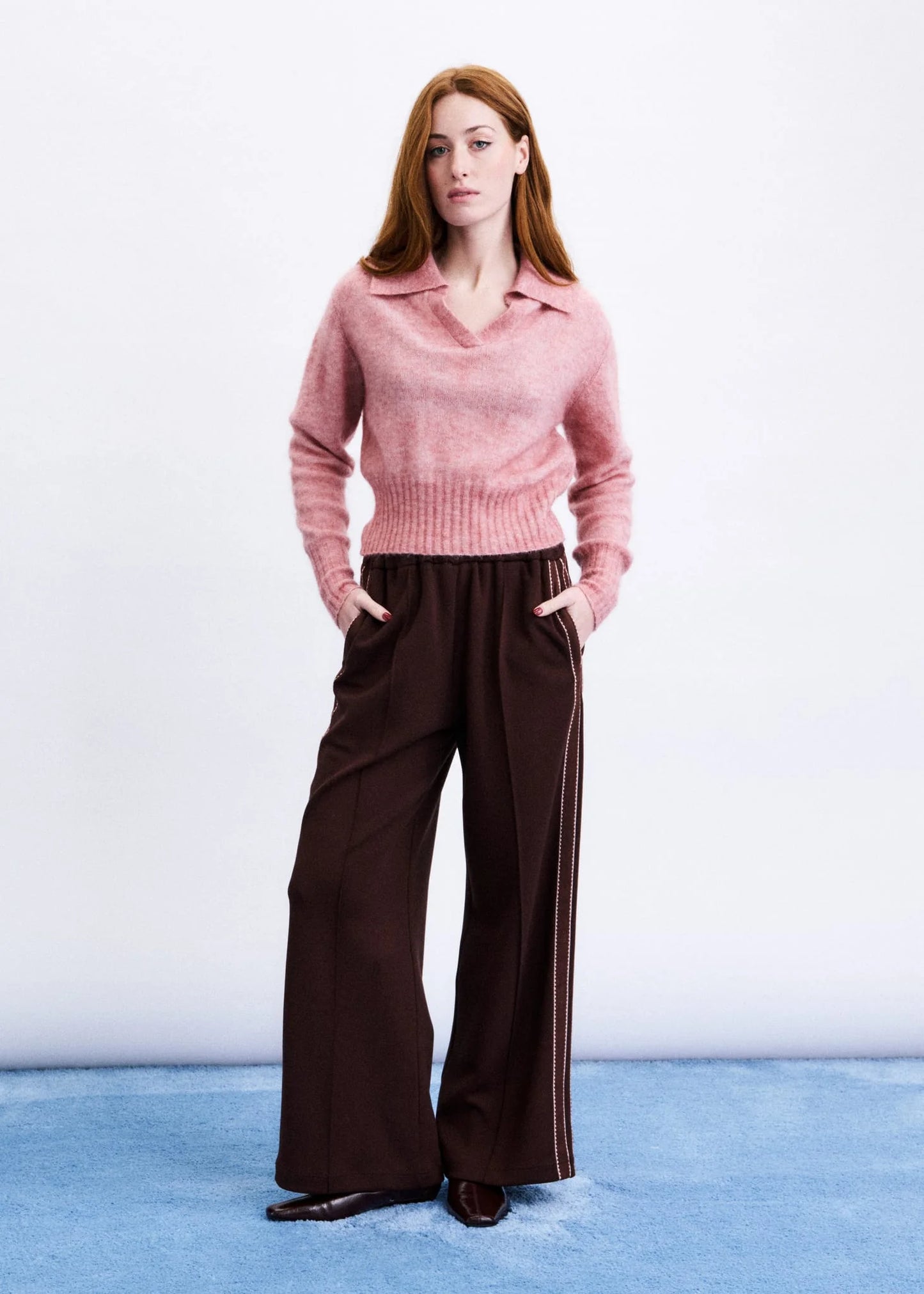 Woman wearing a pink sweater and brown pants on a white background