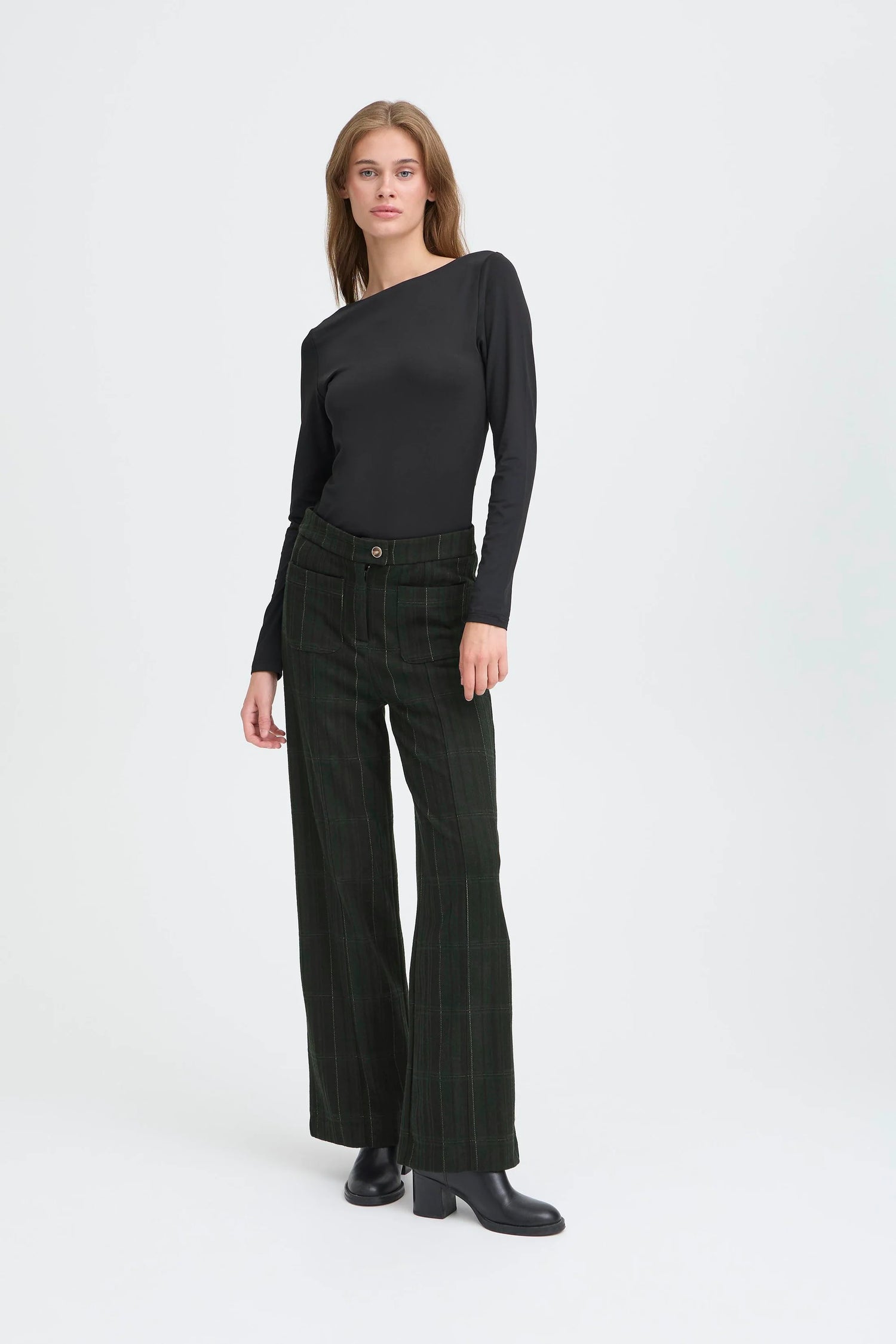 Woman wearing a black top and dark plaid pants on a white background