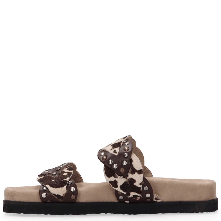 Pair of sandals with cow print straps on a beige sole against a white background