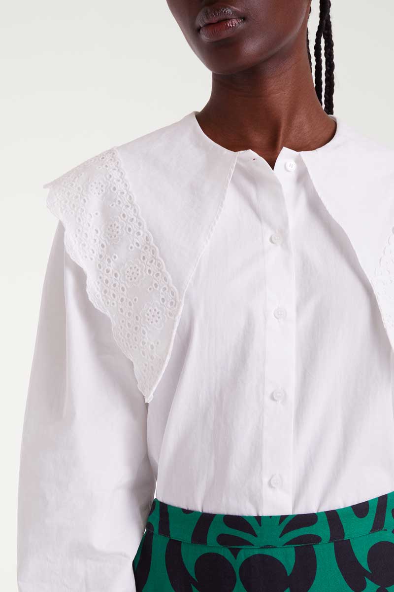 White blouse with intricate collar design worn by a person against a white background