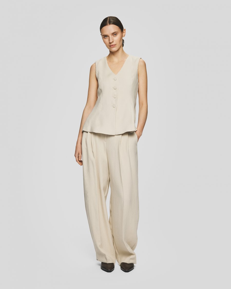 Woman wearing a beige sleeveless top and pants on a light gray background