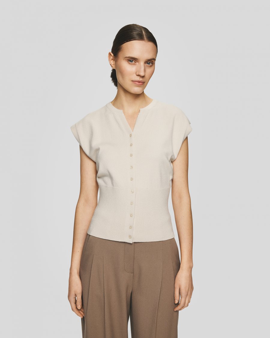 Woman wearing a beige sleeveless top and brown pants on a light gray background