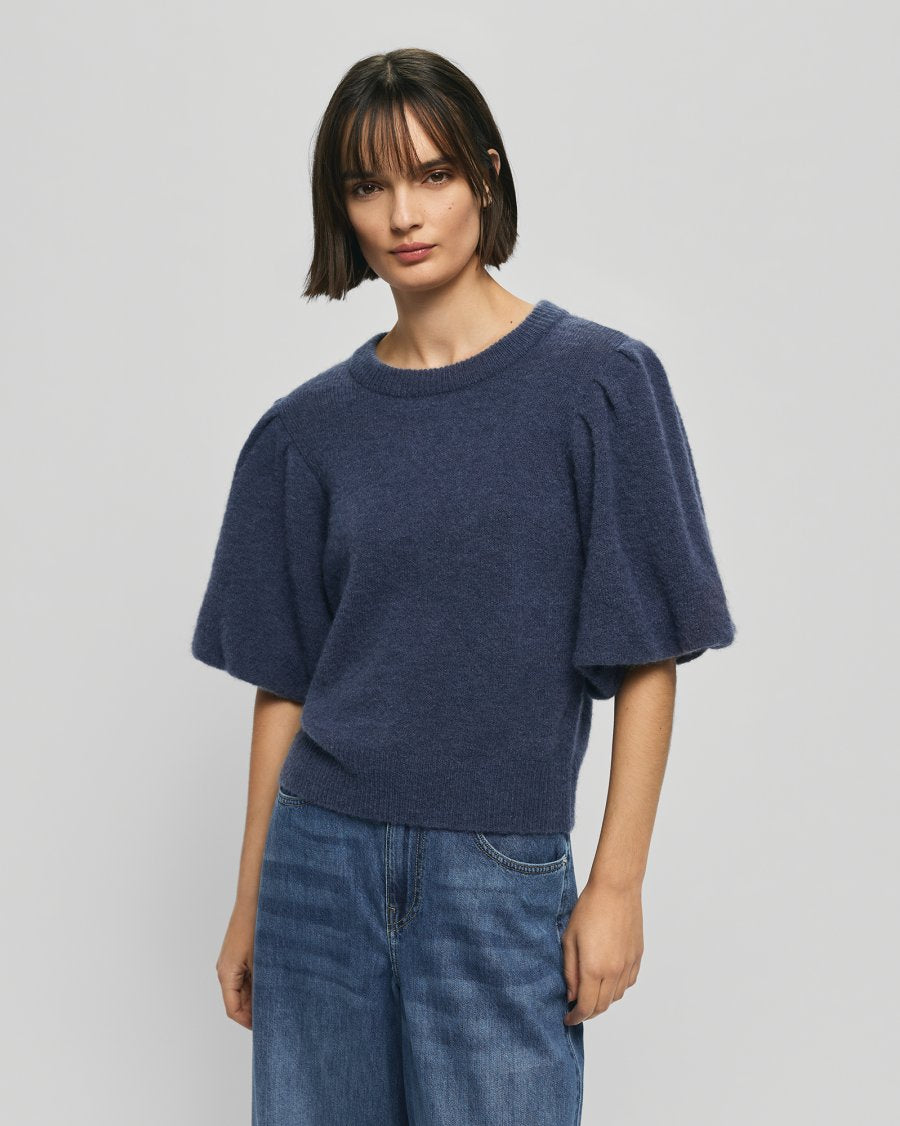 woman wearing a navy pullover and blue jeans standing in front of a white background