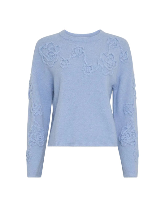 A light blue crewneck sweater featuring raised floral lace applique across the chest and along the sleeves, shown against a solid light gray background.