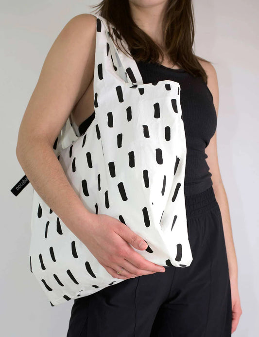 Person holding a white tote bag with black geometric pattern against a plain background