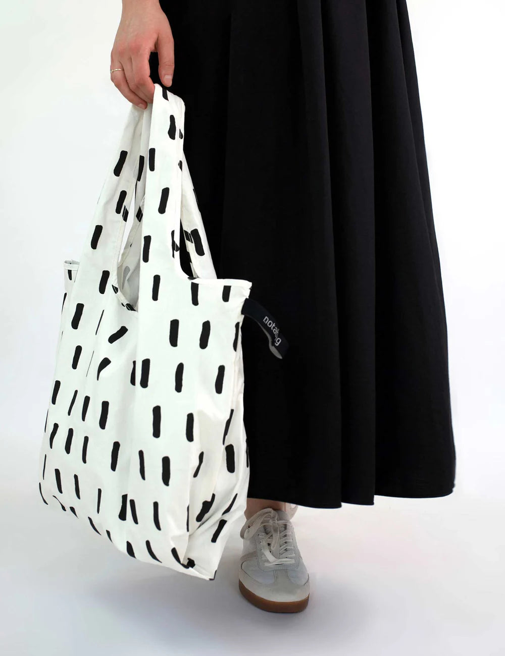 Person holding a white reusable bag with black abstract patterns on a plain background