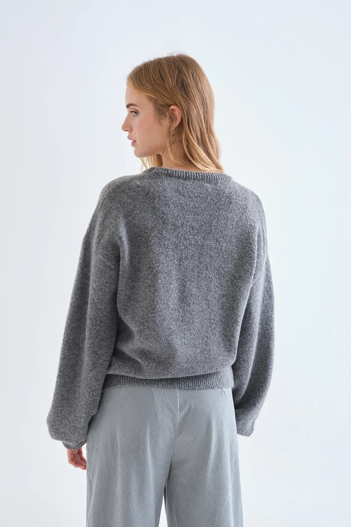 A woman shown from the back wearing a heather gray knit sweater and light gray pants against a plain white studio background.